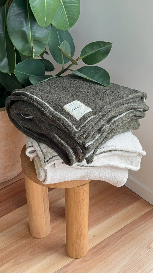 Folded Banksia and Dunes knitted home blankets stacked in warm interior light