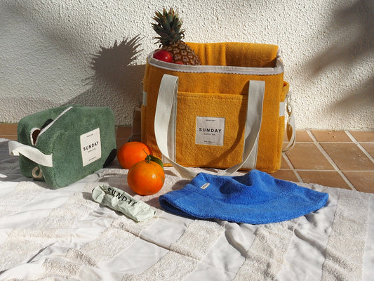 Yellow cooler bag and green pouch beside fruit and a blue towel.