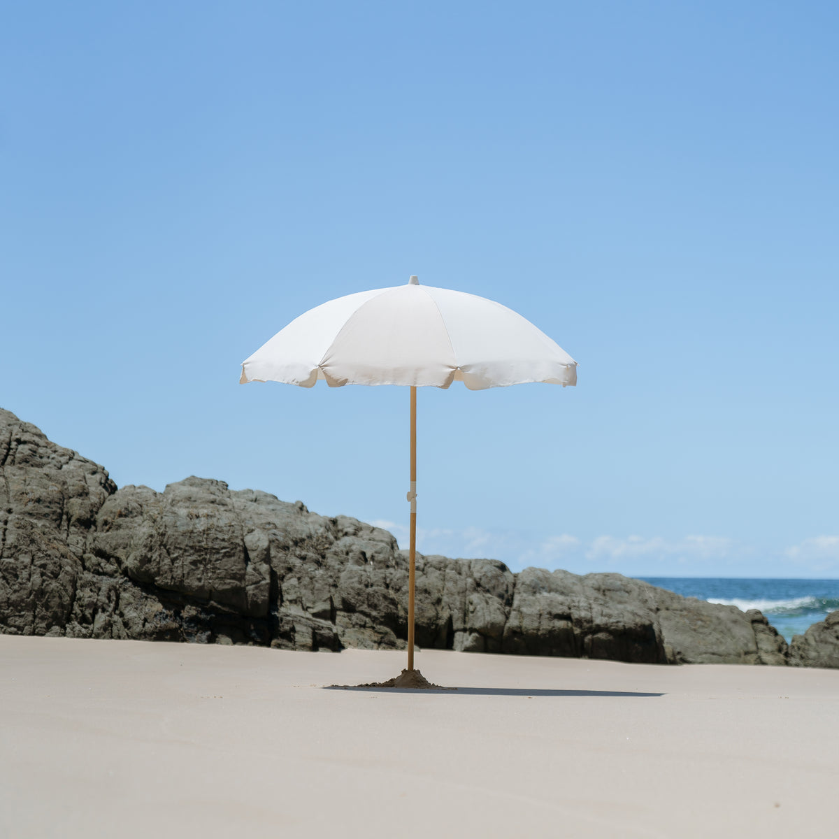 Dunes Splice Beach Umbrella on open sand beside coastal rocks
